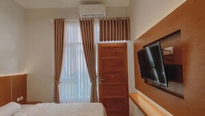 Une chambre d’hôtel avec un lit, un téléviseur fixé au mur, une tête de lit en bois et une porte avec des rideaux.