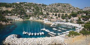 Un puerto costero con barcos amarrados, una costa rocosa y edificios con estructuras abovedadas al fondo.