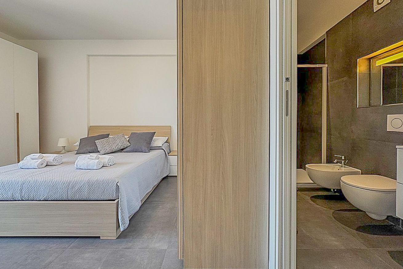 A modern bedroom with a bed, bedside tables, and a bathroom with a sink and toilet.