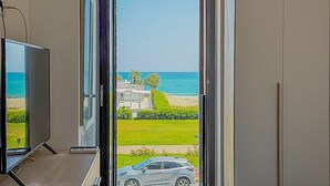 Ein Zimmer mit Fernseher, einer Tür zu einem Balkon mit Meerblick und einem abgestellten Auto.