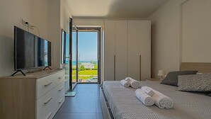 Ein Schlafzimmer mit Fernseher, einem Bett mit zusammengerollten Handtüchern, einem Kleiderschrank und Meerblick.