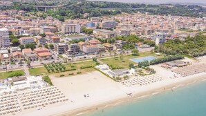 Luftaufnahme einer Küstenstadt mit Strand, Hotelgebäuden und einer Brücke im Hintergrund.