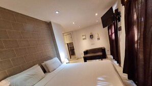 Habitación de hotel con una cama grande, un escritorio, una silla y un televisor montado en la pared.