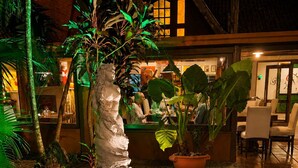 Un patio con una estatua, plantas en macetas y un edificio de fachada de madera.