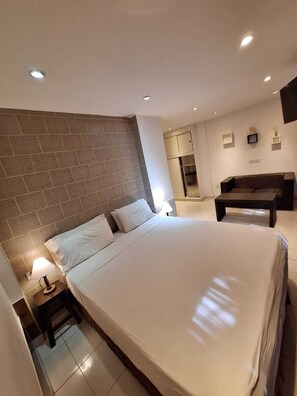 Une chambre d’hôtel moderne avec un grand lit, une petite table, un canapé et un coin cuisine.