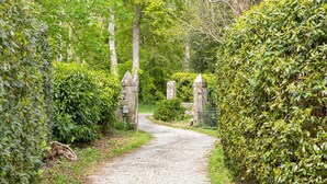 Un camino de grava bordeado por setos verdes frondosos y estructuras de piedra.