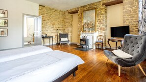 Un dormitorio con cama, un sillón gris, una pared de piedra, chimenea y televisor.