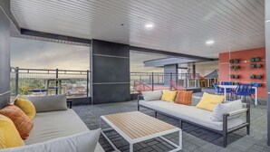 Ein Außenbereich mit Sitzgelegenheiten, darunter eine Couch, ein Tisch und Stühle, ein Balkon mit Geländer sowie Blick zum Himmel.