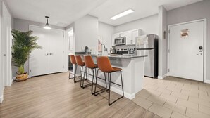 Eine moderne Küche mit weißen Schränken, einer zentralen Kochinsel mit Barhocker und einem Blumentopf.