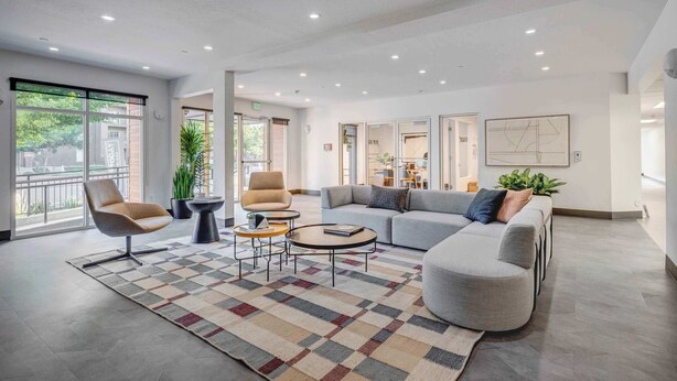Eine moderne Lobby mit einer grauen Couch, Sesseln und einem gemusterten Teppich.