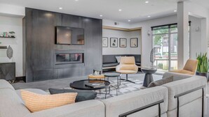 Ein modernes Wohnzimmer mit einer Sofagarnitur, einem Couchtisch und zwei Sesseln. Ein Flachbildfernseher ist an der Wand montiert, darunter befindet sich ein Kamin.