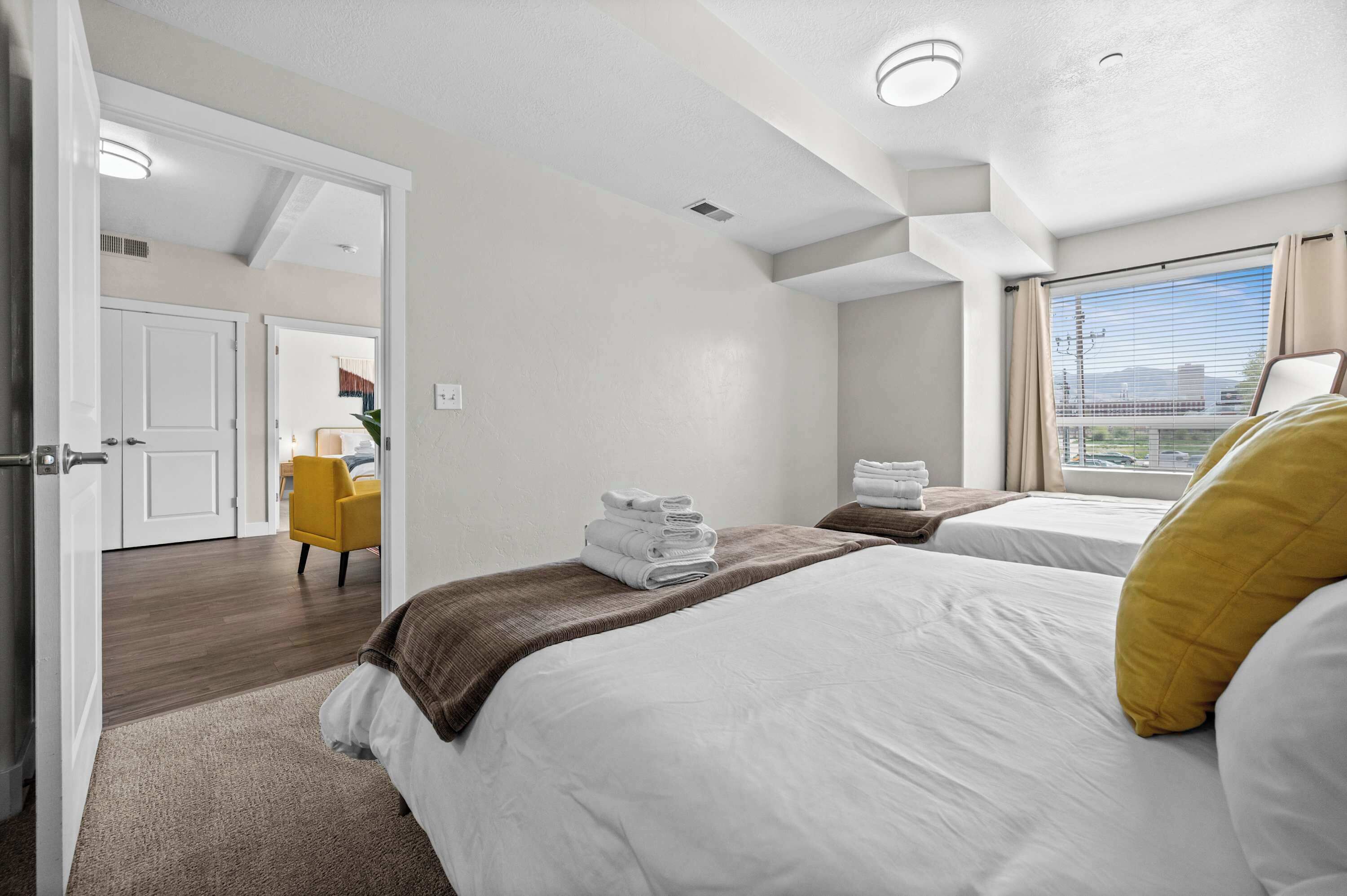 A hotel room with two beds, a view of the city, and a yellow chair.