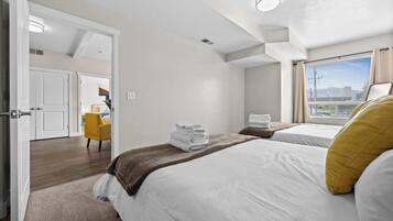 A hotel room with two beds, a view of the city, and a yellow chair.