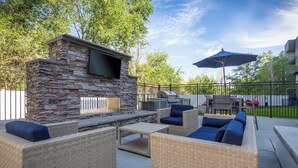 Eine Terrasse im Freien mit Steinen und Rattanmöbeln, einem Flachbildfernseher und einem Grill.