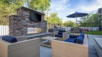 An outdoor patio with stone and wicker furniture, a flat-screen TV, and a grill.