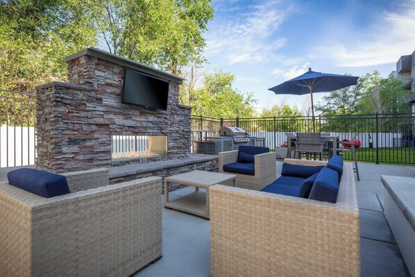 Un patio al aire libre con mobiliario de piedra y mimbre, un televisor de pantalla plana y una parrilla.