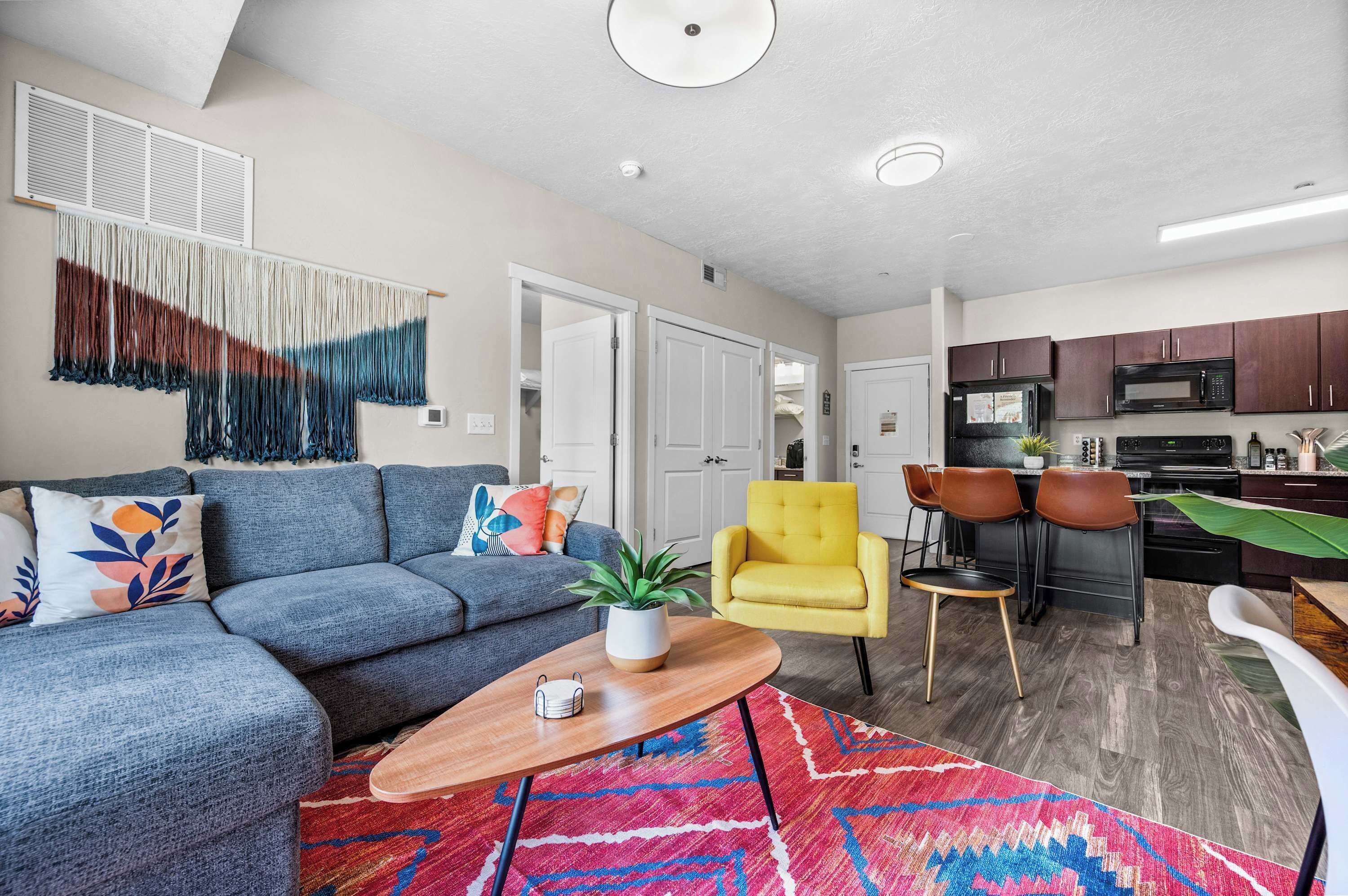 A living room with a sofa, coffee table, and chairs, a kitchen with appliances, and a dining area with chairs.