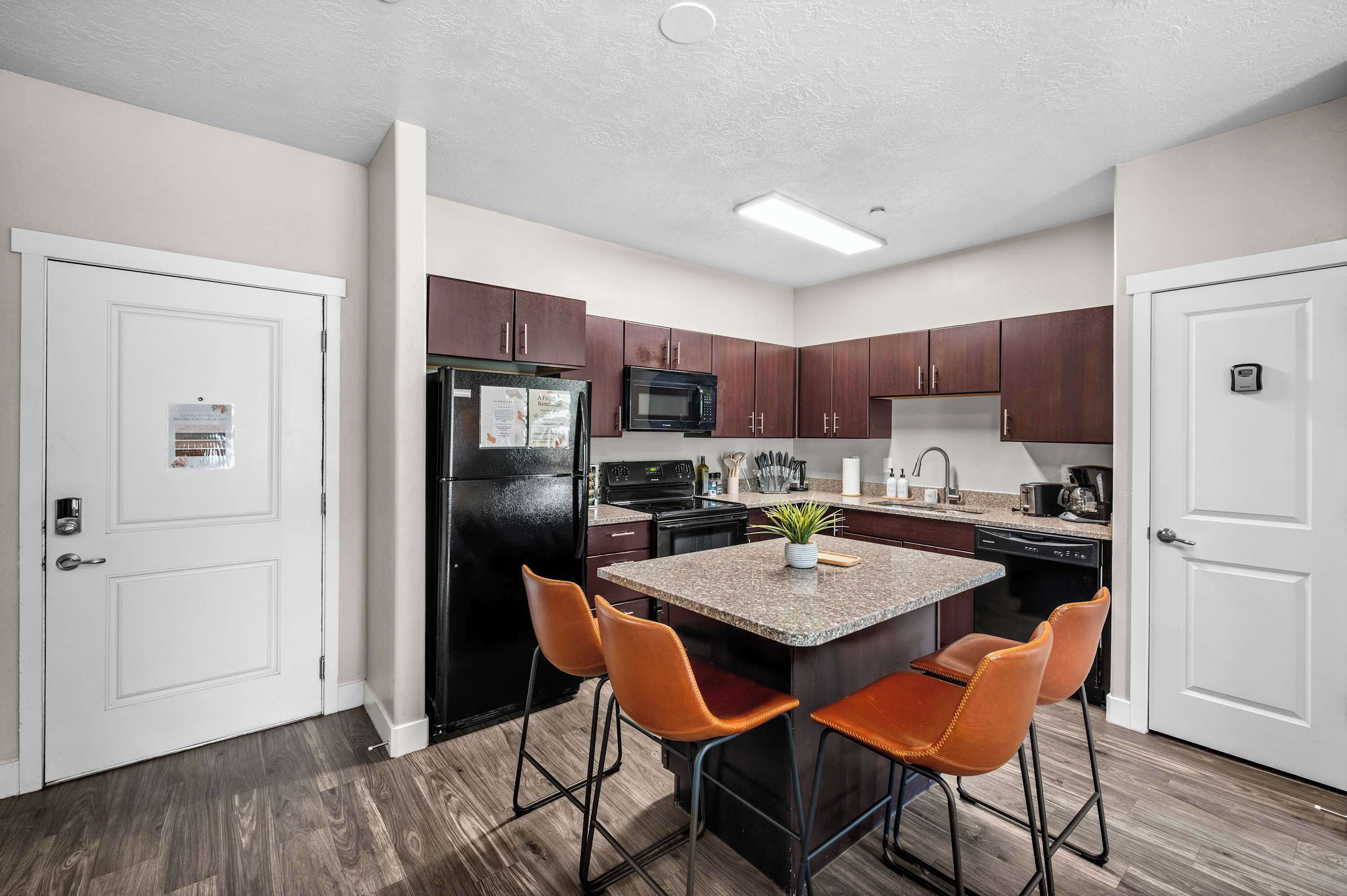 A modern kitchen with a central island, two bar stools, and wooden flooring.