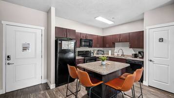 A modern kitchen with a central island, two bar stools, and wooden flooring.