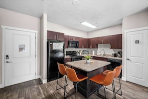 A modern kitchen with a central island, two bar stools, and wooden flooring. - Downtown SLC 2BR Delta & Conference (Salt Lake City)