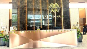 A reception desk with a modern design, featuring a marble-like facade and a logo above the name 'THE MANOR.' - THE MANOR CLASIC SUITES BY BUKIT BINTANG (Kuala Lumpur)