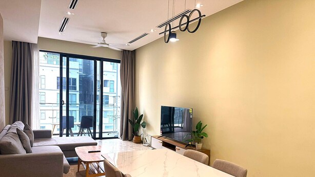A modern living room with a sofa, a dining table, chairs, a TV, and a balcony with a view of buildings. - THE MANOR CLASIC SUITES BY BUKIT BINTANG (Kuala Lumpur)