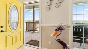Una puerta amarilla con un panel de vidrio, una terraza de madera y una pared decorativa con motivos de peces y tortugas.