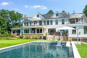 A large, two-story house with a swimming pool, stone accents, and a well-maintained lawn.