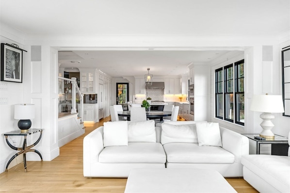 A modern living room with a white sofa, a dining area, and a kitchen in the background.