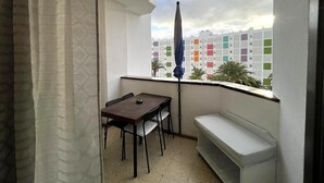 Een balkon met een tafel en stoelen, een bankje, uitzicht op kleurrijke gebouwen en een heldere lucht.