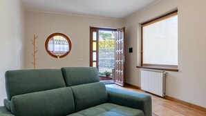 Una habitación con un sofá verde, un perchero de madera, una ventana con vistas y un radiador.