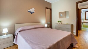 Un dormitorio con cama, mesita de noche, cómoda, espejo y lámpara fijada a la pared.