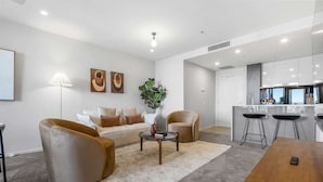 A modern living room with a sofa, two armchairs, a coffee table, and a dining table. - Bright Apartment With Pool and Gym Access (Brisbane)