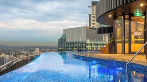 A modern building with a rooftop infinity pool, glass facade, and a view of the cityscape. - Bright Apartment With Pool and Gym Access (Brisbane)