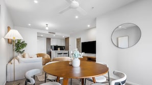 A modern dining area with a round wooden table, grey upholstered chairs, a floor lamp, and a ceiling fan. - Bright Apartment With Pool and Gym Access (Brisbane)