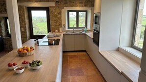 Cozinha moderna com parede de pedra, uma janela ampla e uma ilha de madeira com cestos de frutas.