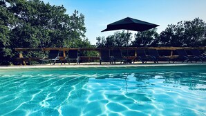 A clear pool with visible ripples, surrounded by lounge chairs and an umbrella.