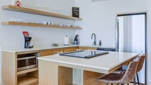 Een moderne keuken met een centraal eiland, houten kasten, een roestvrijstalen afzuigkap en een koelkast.