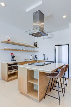 Eine moderne Küche mit einer zentralen Kochinsel, Holzschränken, einer Edelstahl-Dunstabzugshaube und einem Kühlschrank.