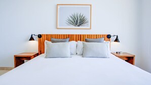 Een net opgemaakt bed met twee kussens, een houten hoofdbord en twee nachtkastjes met lampen.