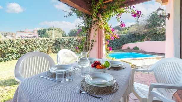 An outdoor dining area with a table set for two, surrounded by white chairs, a pool in the background, and a pergola with climbing plants. - Villa 'Armonia - Private Pool' with Private Pool, Wi-Fi and Air Conditioning (Punta de Su Turrione)