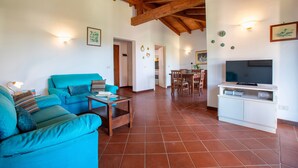 A living room with a sofa, a coffee table, a TV on a stand, and a dining area in the background. - Villa 'Armonia - Private Pool' with Private Pool, Wi-Fi and Air Conditioning (Punta de Su Turrione)