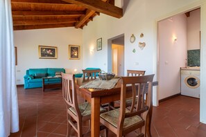 Une salle à manger avec des chaises et une table en bois, un salon avec un canapé de couleur turquoise et une buanderie équipée d’un lave-linge.