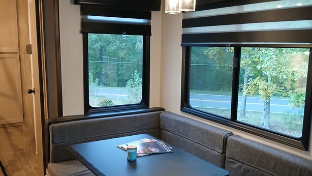 Ein gemütliches Wohnmobil-Interieur mit einer Sitzecke, einem Tisch und großen Fenstern, die einen Blick ins Freie ermöglichen.