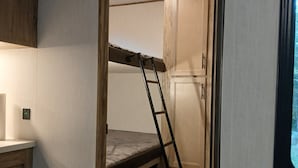Ein kleines Zimmer mit Etagenbett, einer Klapptreppe, einem kleinen Schreibtisch und einem Fenster.