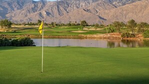 Un parcours de golf avec un drapeau, un étang et des montagnes en arrière-plan.