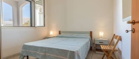 Un dormitorio con cama, mesitas de noche, una silla y una ventana.
