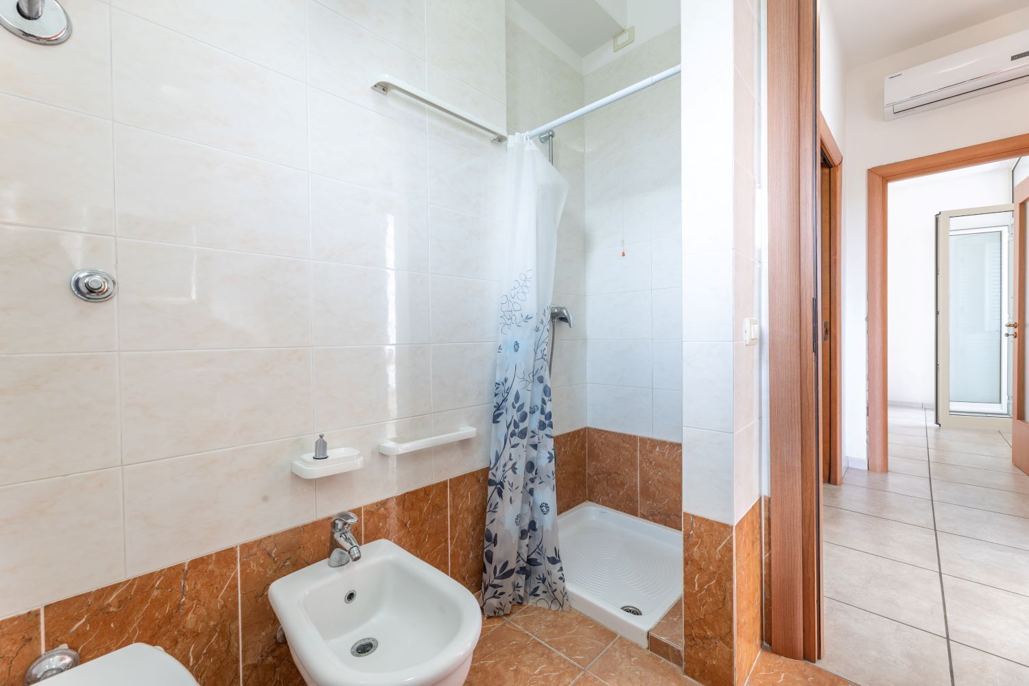 Un bagno con doccia, due lavandini e il water.