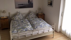 A bed with floral bedding, two bedside tables with lamps, a framed picture on the wall, and a door to the right. - Apartment "Lindau" with Shared Terrace, Garden, and Wi-Fi (Uhldingen-Mühlhofen)