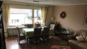 A living room with a dining area, a sofa, a table with a book, and a window with curtains. - Apartment "Lindau" with Shared Terrace, Garden, and Wi-Fi (Uhldingen-Mühlhofen)